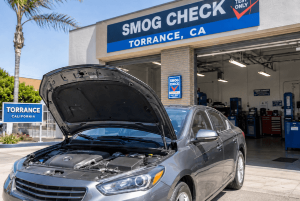 A calm driver confidently pulling into a professional smog testing station in Torrance, California. Show the moment of arrival with the testing facility visible and welcoming. Include subtle visual elements of vehicle maintenance (open hood showing clean engine, fuel cap being checked).
