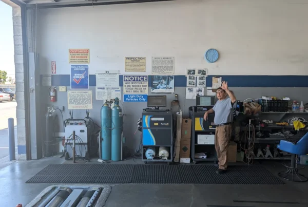 Technician performing a smog inspection on a vehicle connected to diagnostic equipment inside a clean STAR certified smog check station in Southern California.