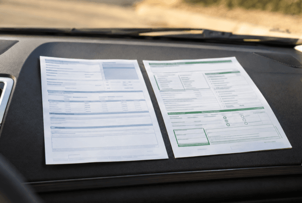 California vehicle registration renewal notice and smog inspection report arranged on a sunlit car dashboard.